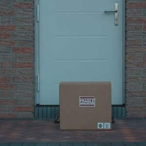 Cardboard box placed outside a brick-walled entrance, labeled fragile for delivery.